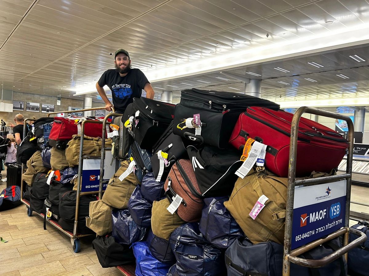 Man smiling behind carts loaded with numerous suitcases at an airport